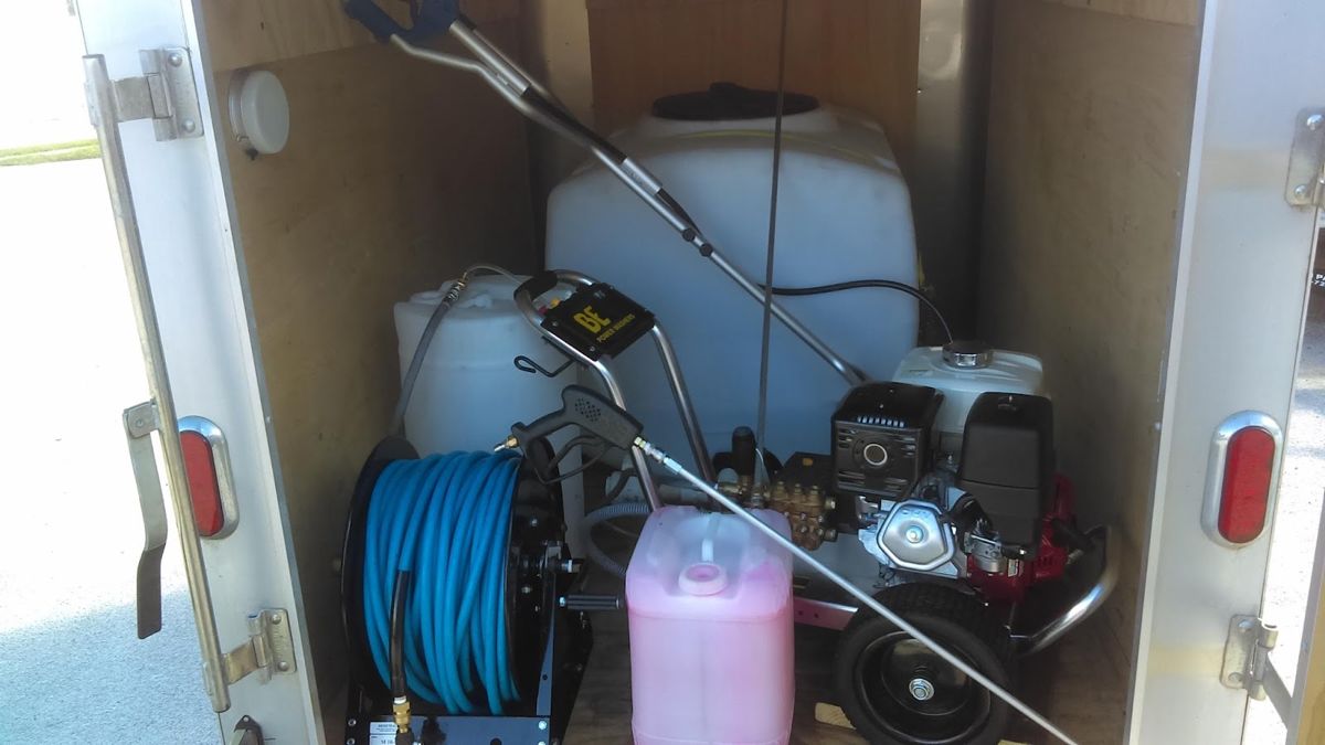 Equipment trailer interior with a pressure washer, hose reel and chemical jug